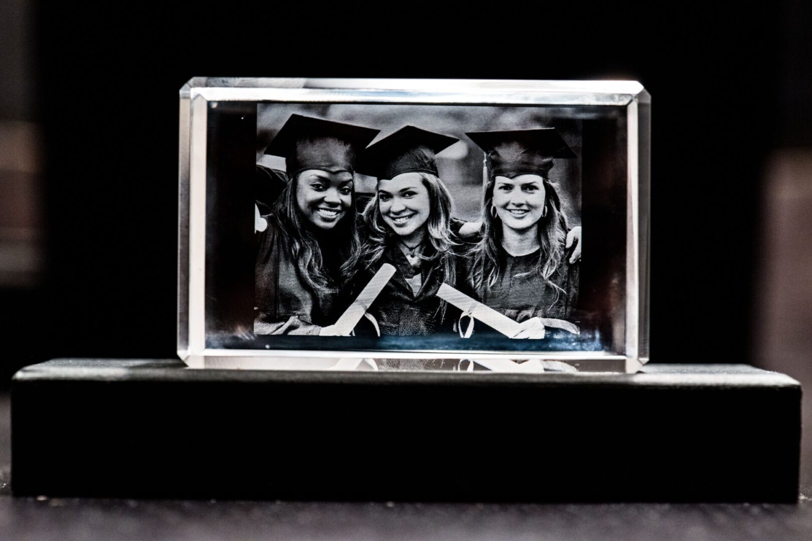 Black-and-white photo of three smiling graduates in a glass frame.